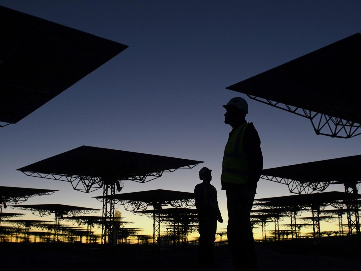 A worker stands next to heliostats. With a total weight of 1.8 tons each, there are 10,600 heliostats (mirrors), which concentrate solar radiation onto the solar receiver, located at the top of a 250-meter-high tower.