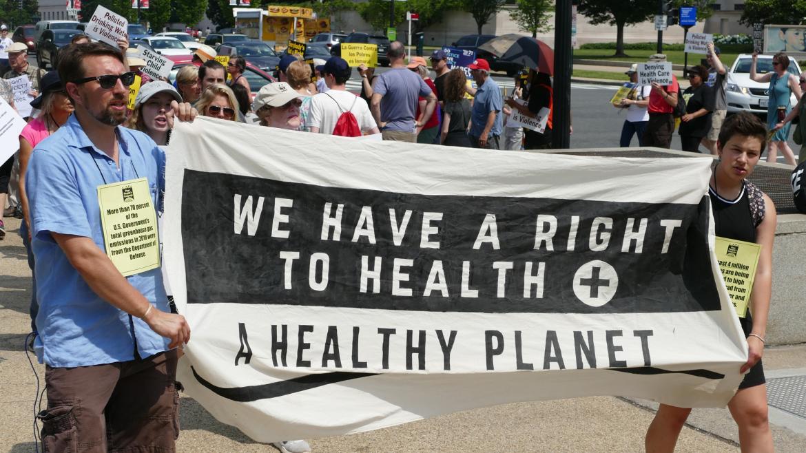 Protestors march holdnig a sign that says "we have a right to health + a healthy planet"